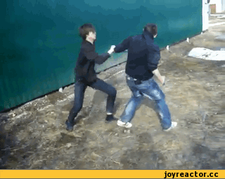 Двое молодых людей дерутся на улице рядом с забором.