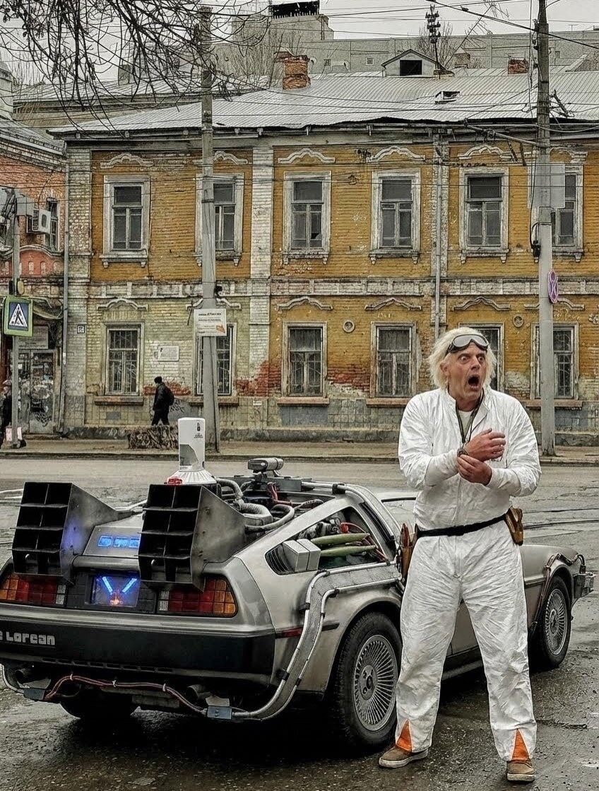 Человек в белом костюме рядом с DeLorean на фоне старинного здания