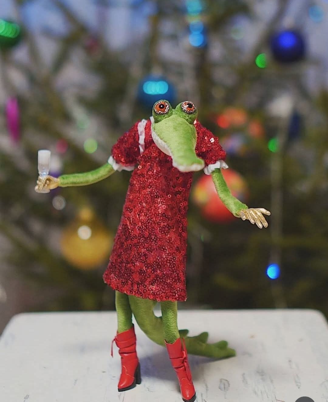 Лягушка-кукла в красном наряде на новогоднем фоне.