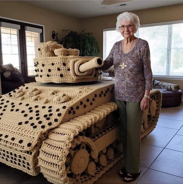 Старшая женщина рядом с огромной вязано-танковой копией.