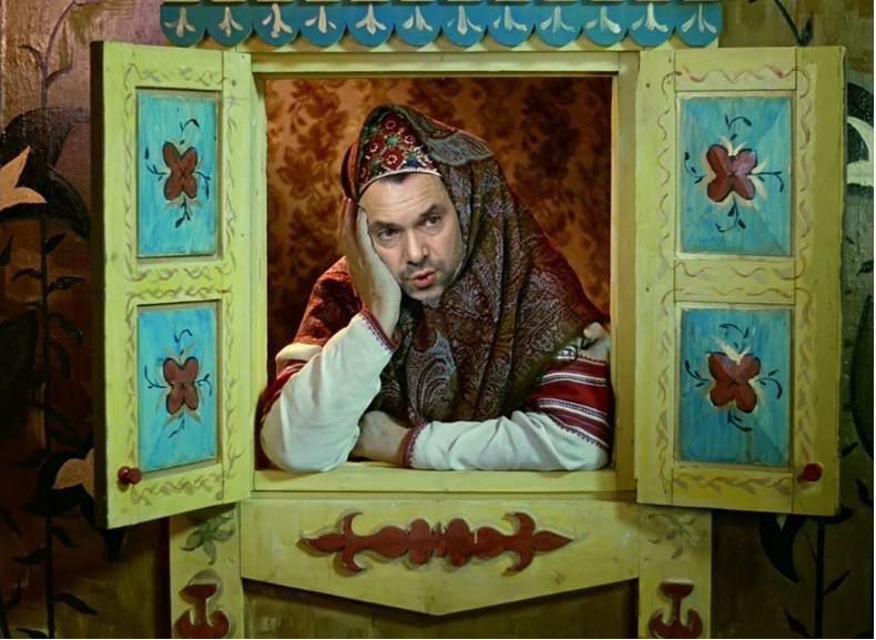 Мужчина смотрит из расписного окна в народной одежде.