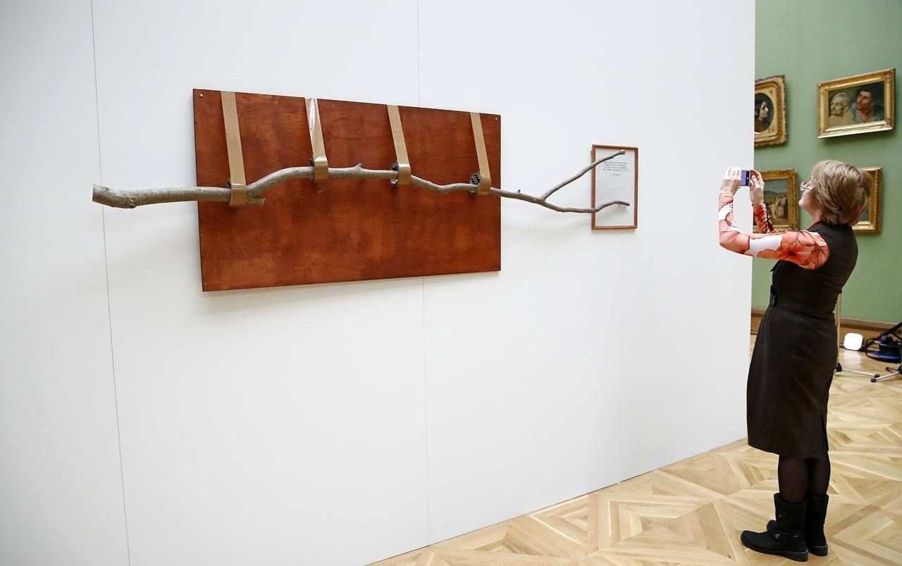 Женщина в галерее фотографирует инсталляцию из ветки, прикреплённую к стене.