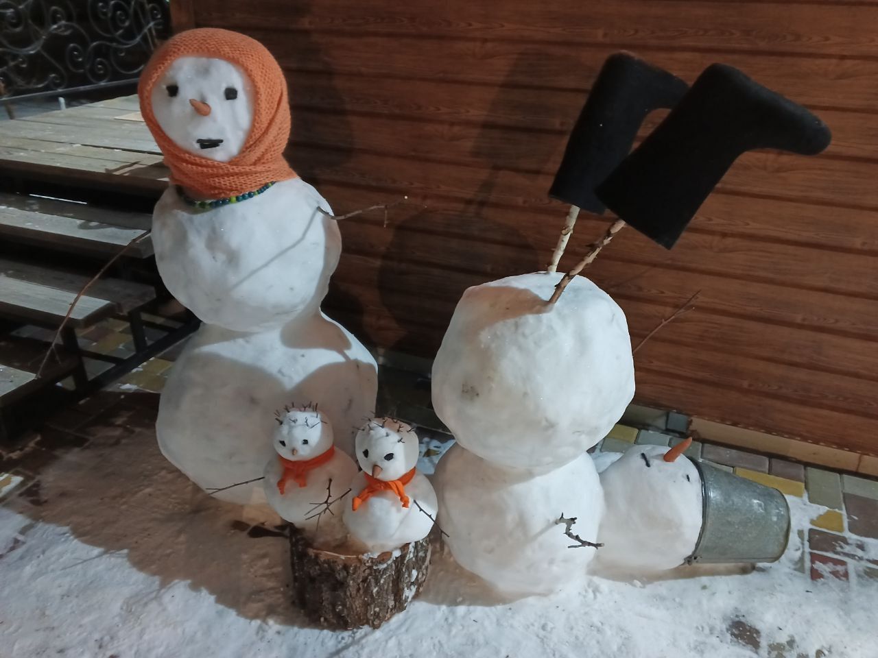 Снежные фигуры: два больших снеговика с шарфами и шляпами, рядом мини-снеговики на бревне.