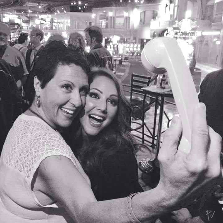 Две женщины улыбаются и делают селфи на фоне кафе.