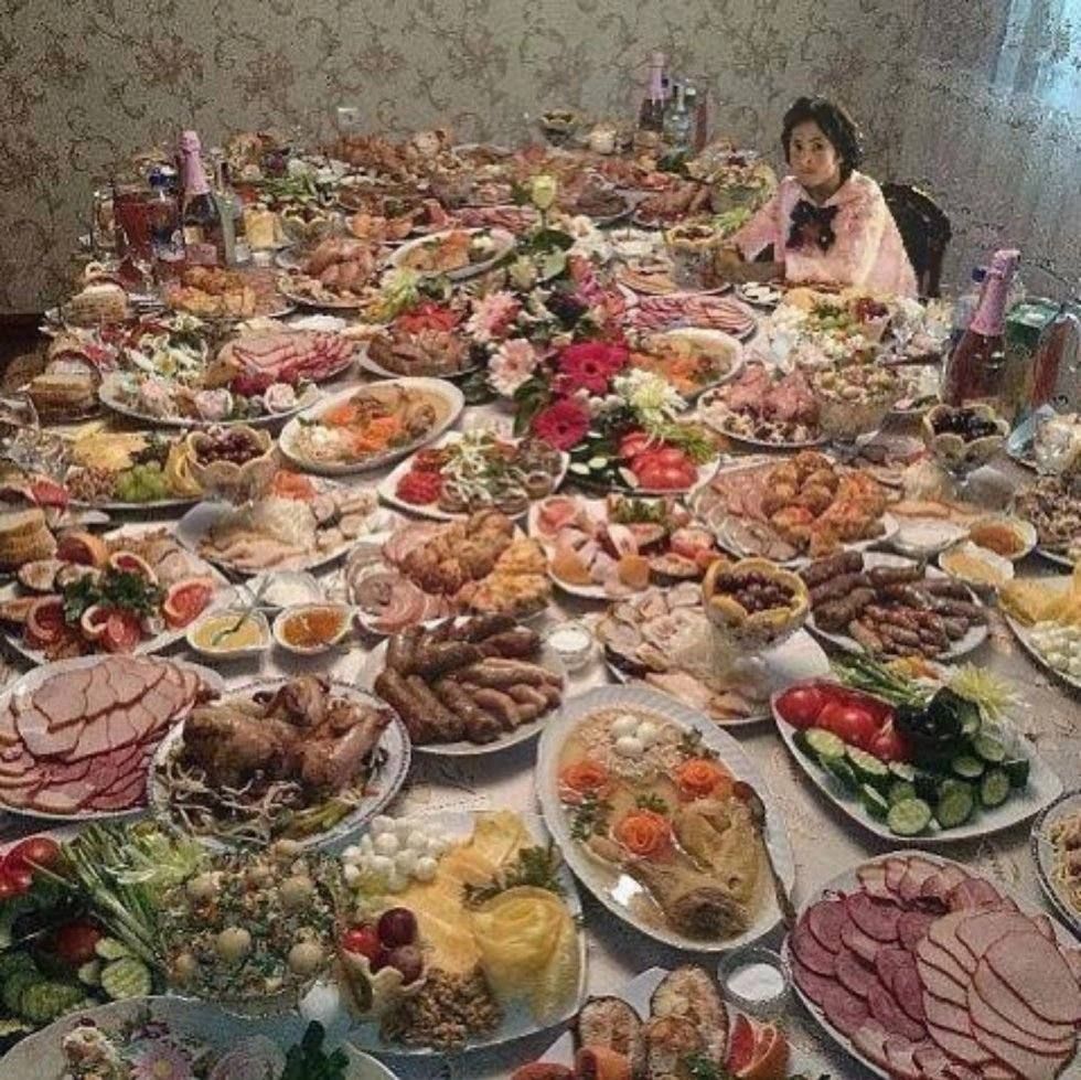 Большой стол с разнообразной едой и девочкой за концом стола.