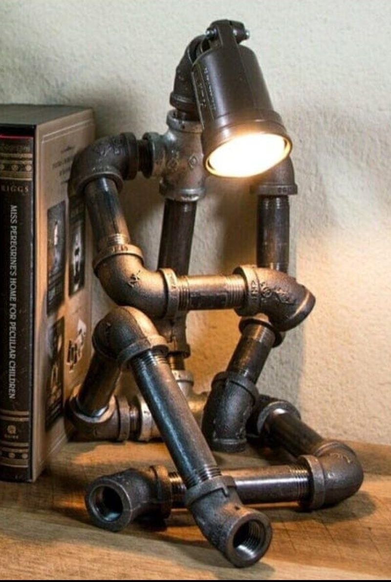Светильник из трубных соединителей на полке рядом с книгой