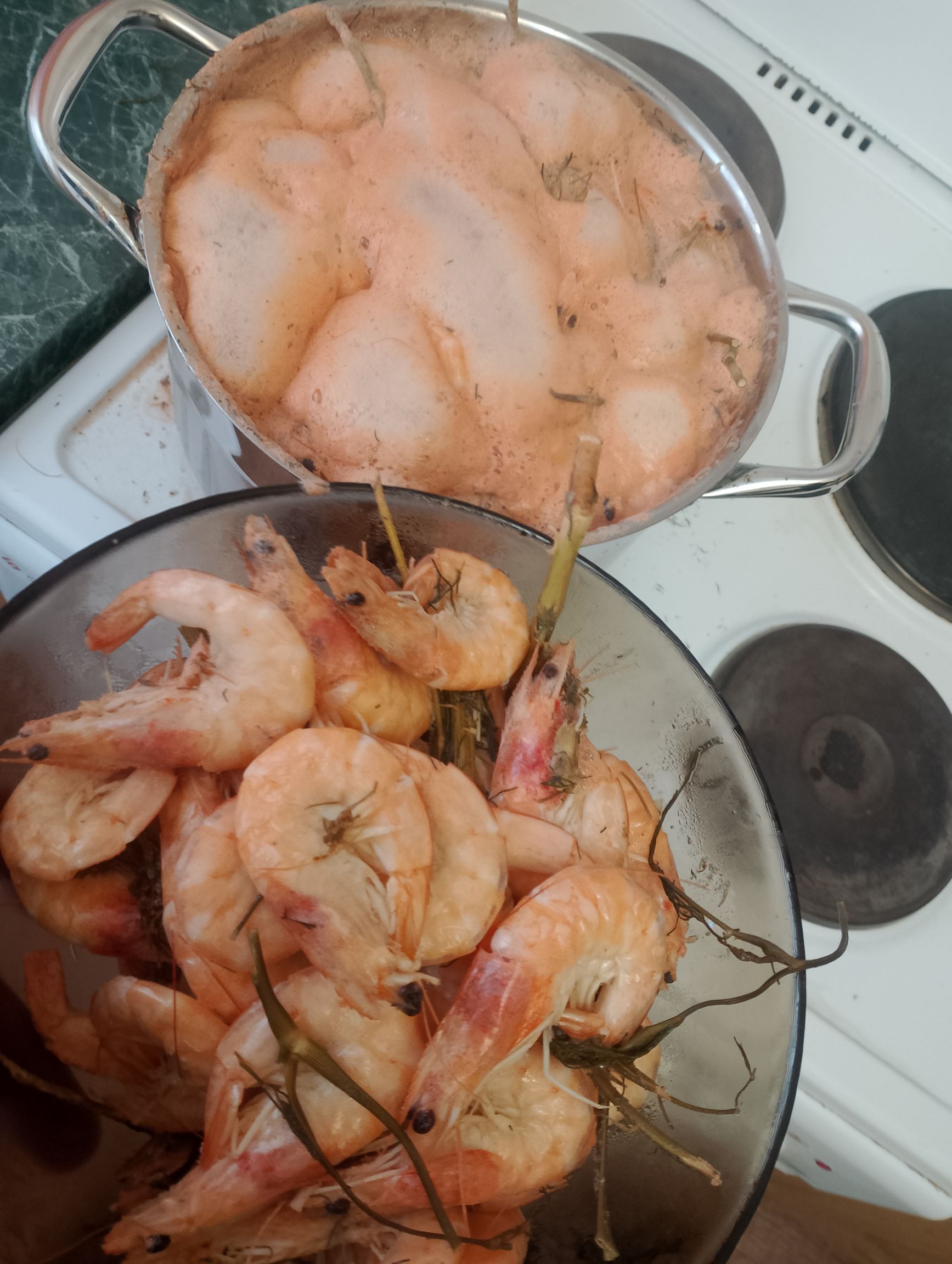 Кастрюля с креветками на плите, рядом большая кастрюля с океанскими креветками.