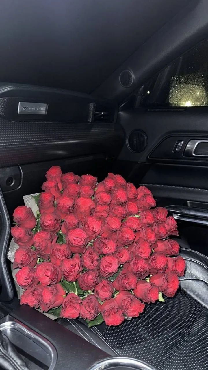 Большой букет красных роз на переднем сиденье авто.