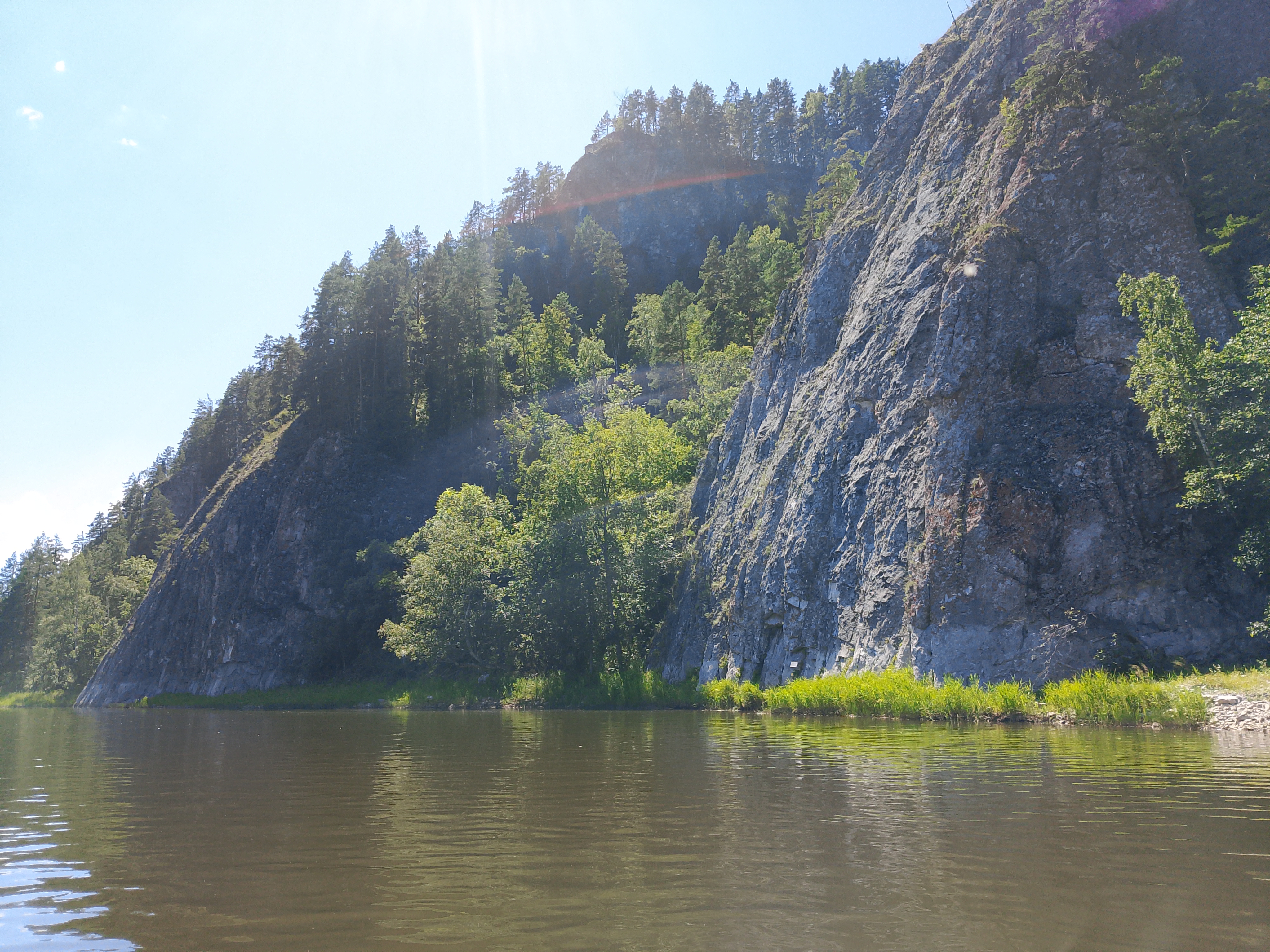 Горная река у подножия скал, поросших деревьями.