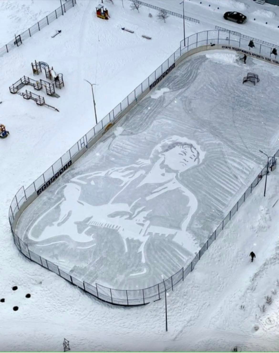 Скульптурное изображение на ледяной дорожке: гигантский портрет человека на снегу на площадке рядом с парком.