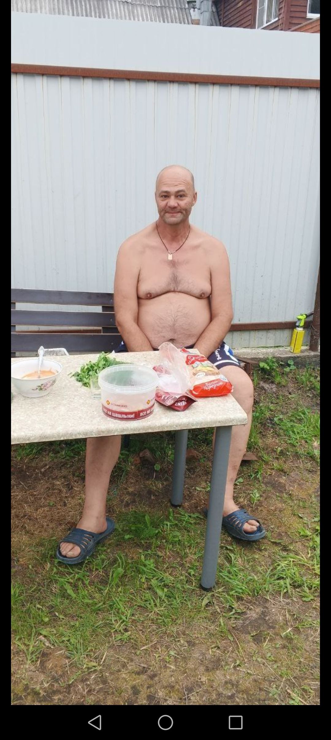 Мужчина без верхней одежды сидит за столом на улице рядом с едой