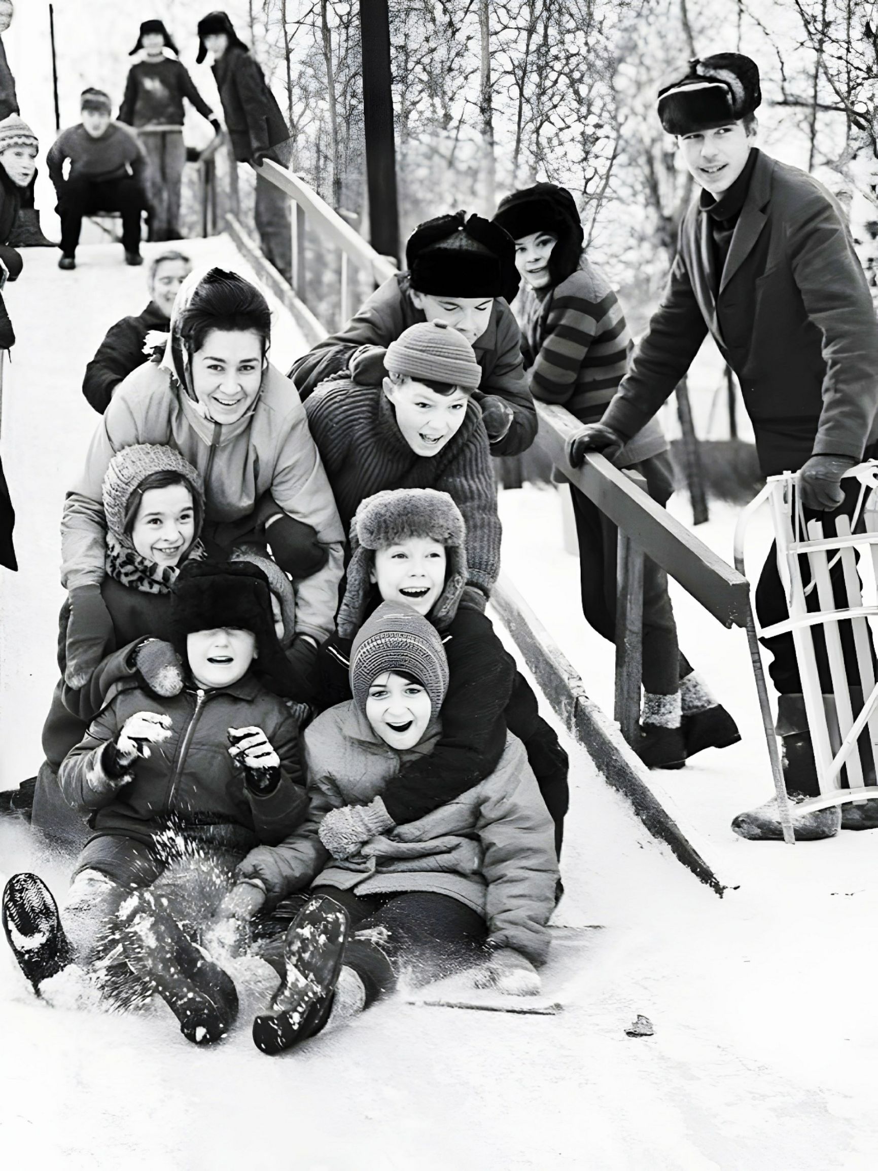 Группа детей и взрослых катятся на санках по заснеженному склону.