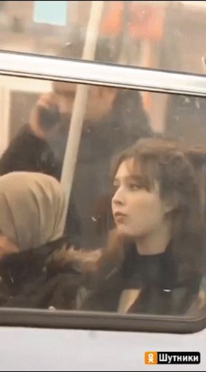 Девушка в черном верхнем одежде сидит в автобусе/поезде рядом с окном