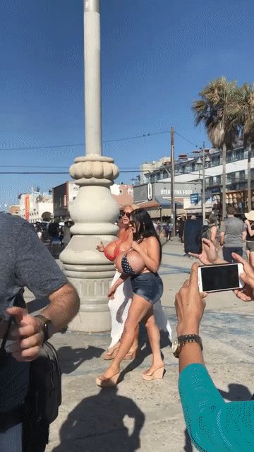 Две девушки в купальниках целуются на набережной, вокруг снимают кадрами прохожие.