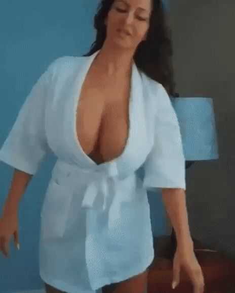 Женщина в белом халате с глубоким декольте, стоит в комнате на синем фоне