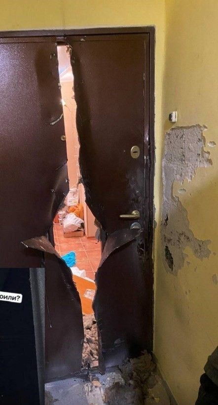 Поврежденная дверь и обвалившаяся штукатурка на стене, беспорядок в помещении.