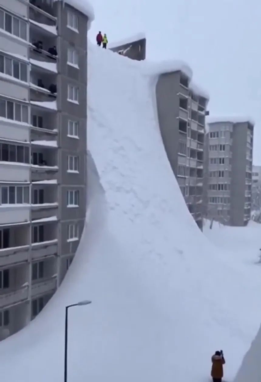 Снежная лавина спускается между жилыми домами, люди стоят на вершине наблюдают