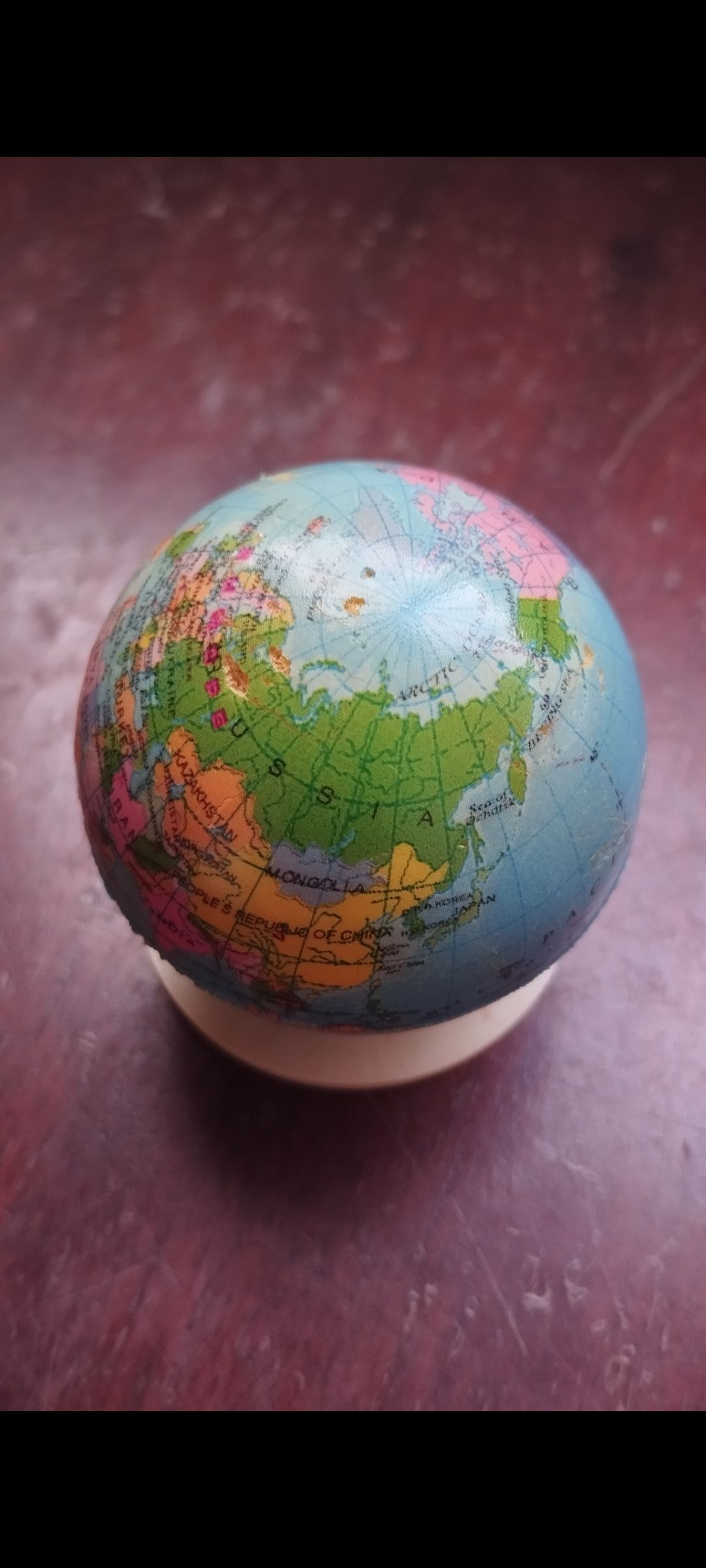 Маленький глобус на подставке на темной поверхности.