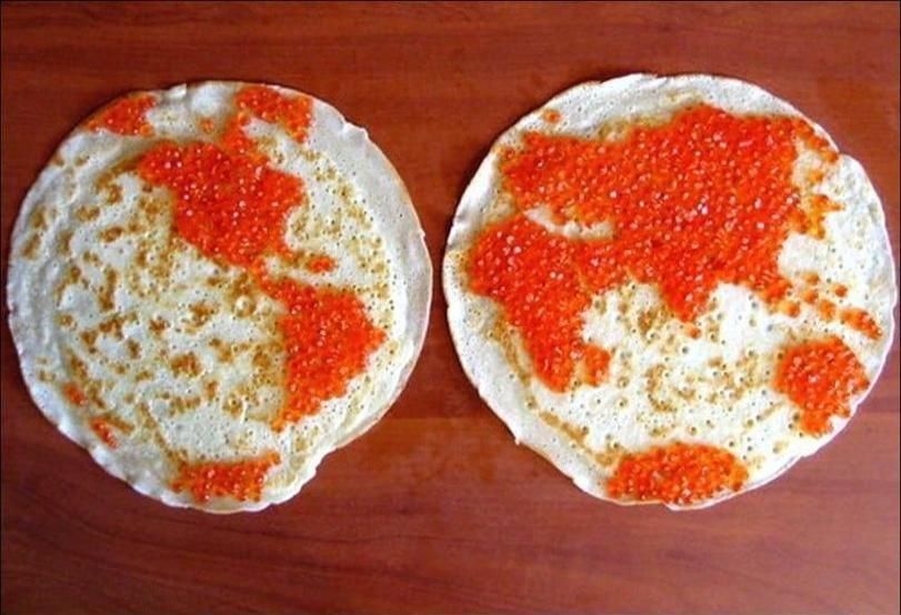 Два круглых хлебца с ярко-оранжевой икрой сверху на деревянной доске.