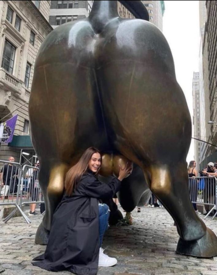 Уличная бронзовая статуя быка с людьми рядом