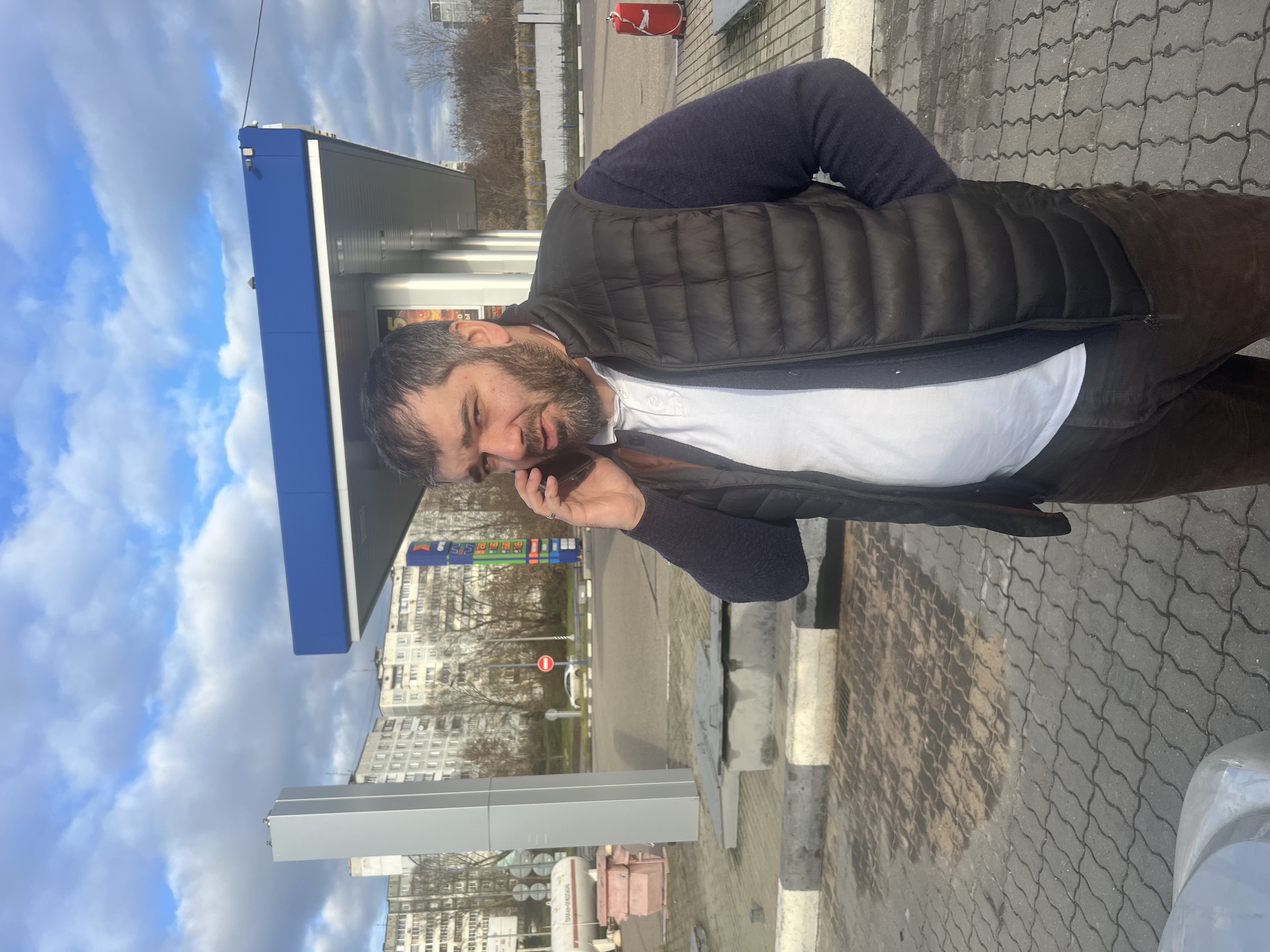 Мужчина стоит у заправочной станции и разговаривает по телефону.