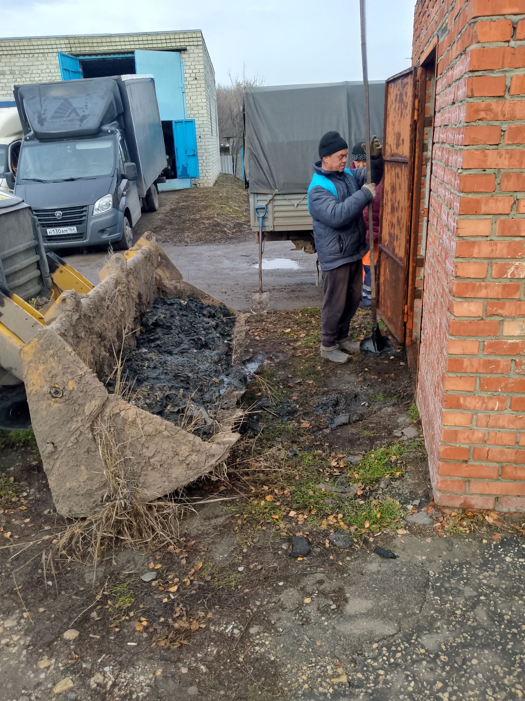 Рабочие возле кирпичной стены, строительная техника и грузовик на улице