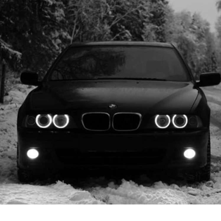 Черный BMW на заснеженной дороге, светятся фары.