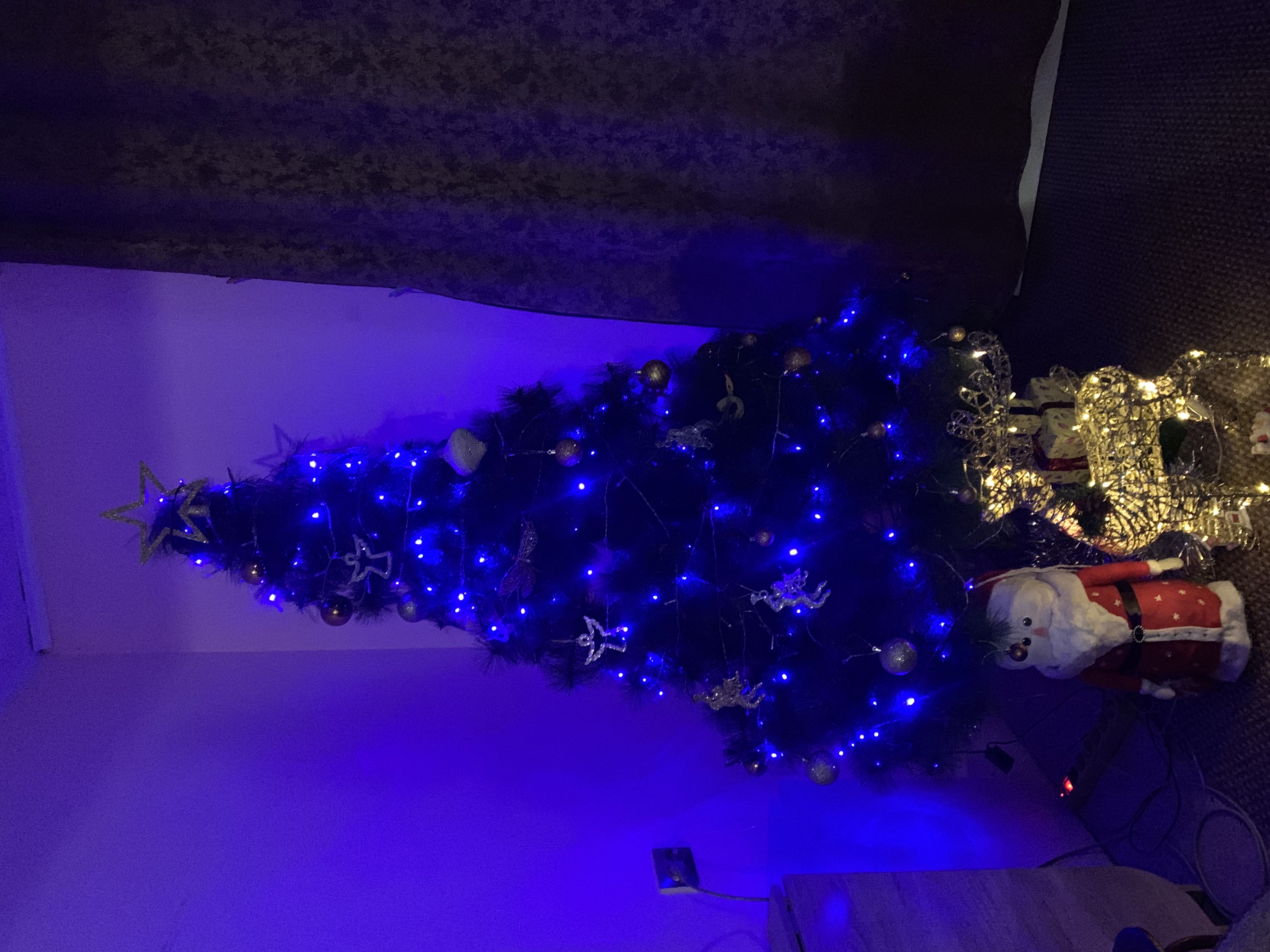 Синяя гирляндная новогодняя ёлка с подсветкой и снежовиком-ouverte на полу.