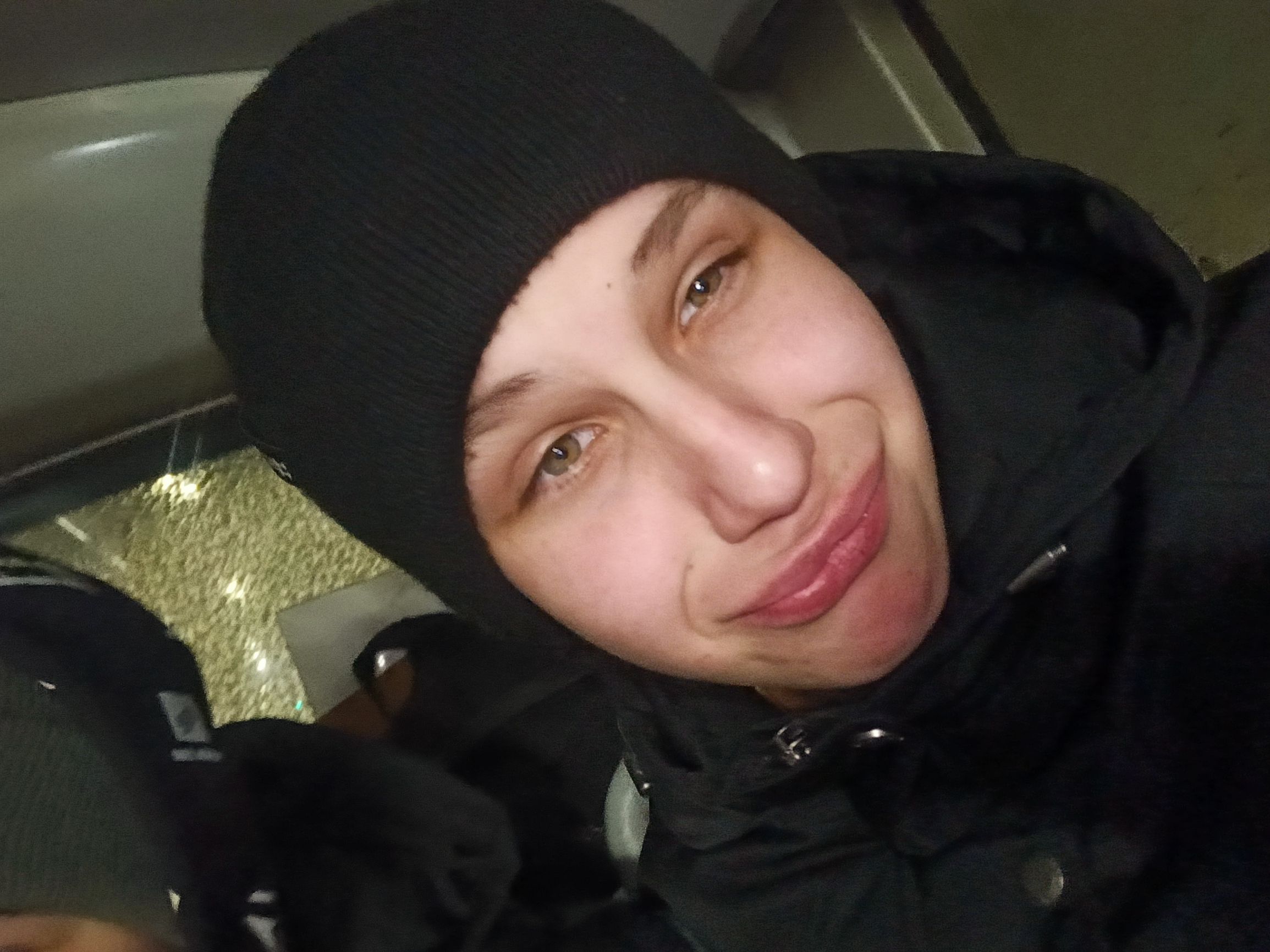 Молодой человек в черной шапке улыбается в автомобиле