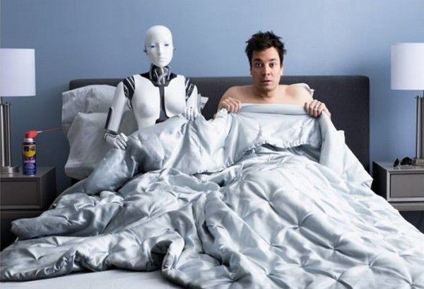 Человек в постели рядом с роботизированным существом.