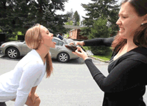 Две женщины на улице: одна подносит еду к рту другой в юмористической сценке.