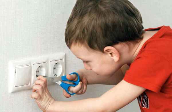 Ребёнок держит ножницы около электрической розетки.