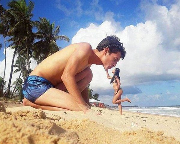 Мужчина копает песок на пляже рядом с ребёнком у моря.