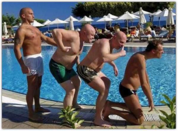 Группа мужчин в плавках выстраивается у бортика бассейна, один из них на коленях возле воды.