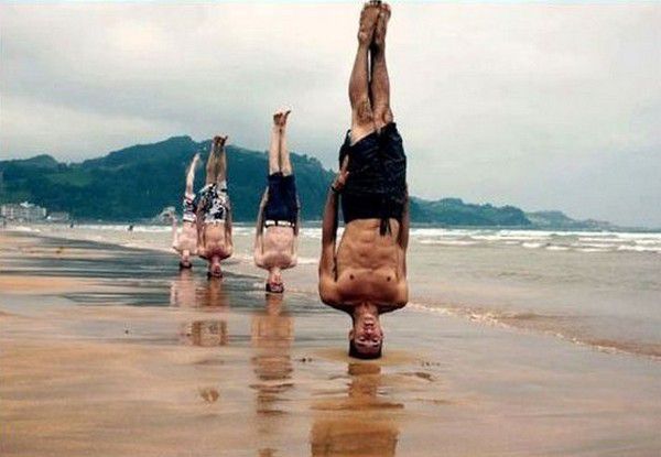 Люди на пляже выполняют стойку на руках в песке.