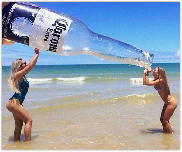 Corona Extra CERVECERIA MODELO S. DE R.L. DE C.V. MEXICO. Две девушки на пляже делают забавную фотографию с гигантской бутылкой пива Corona Extra.