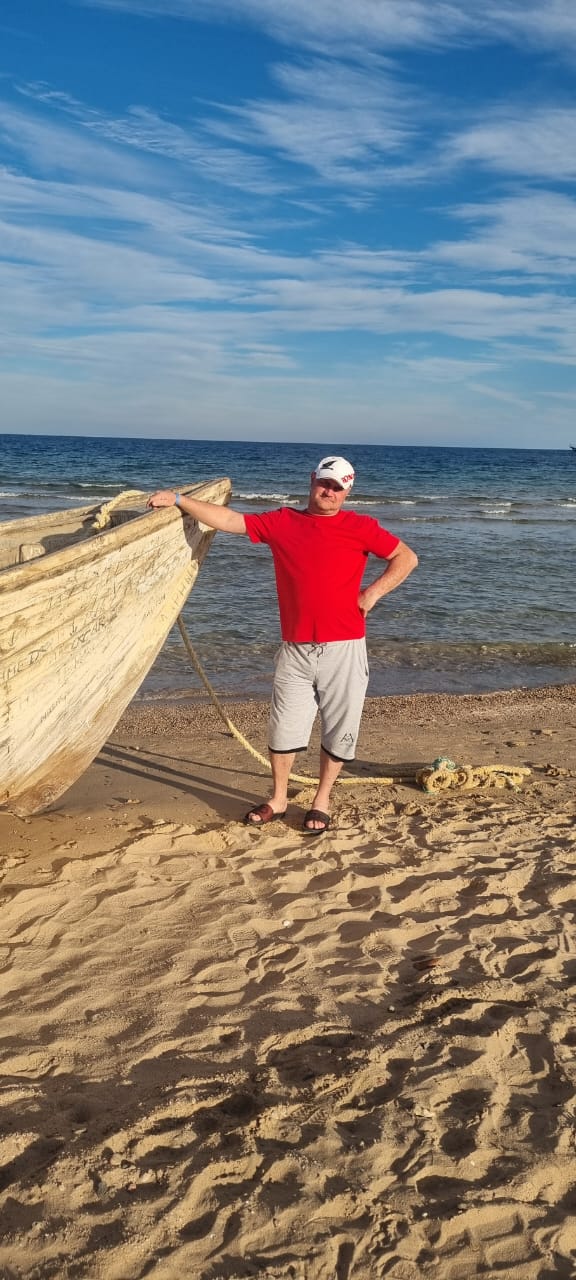 Мужчина на пляже возле старой лодки у моря