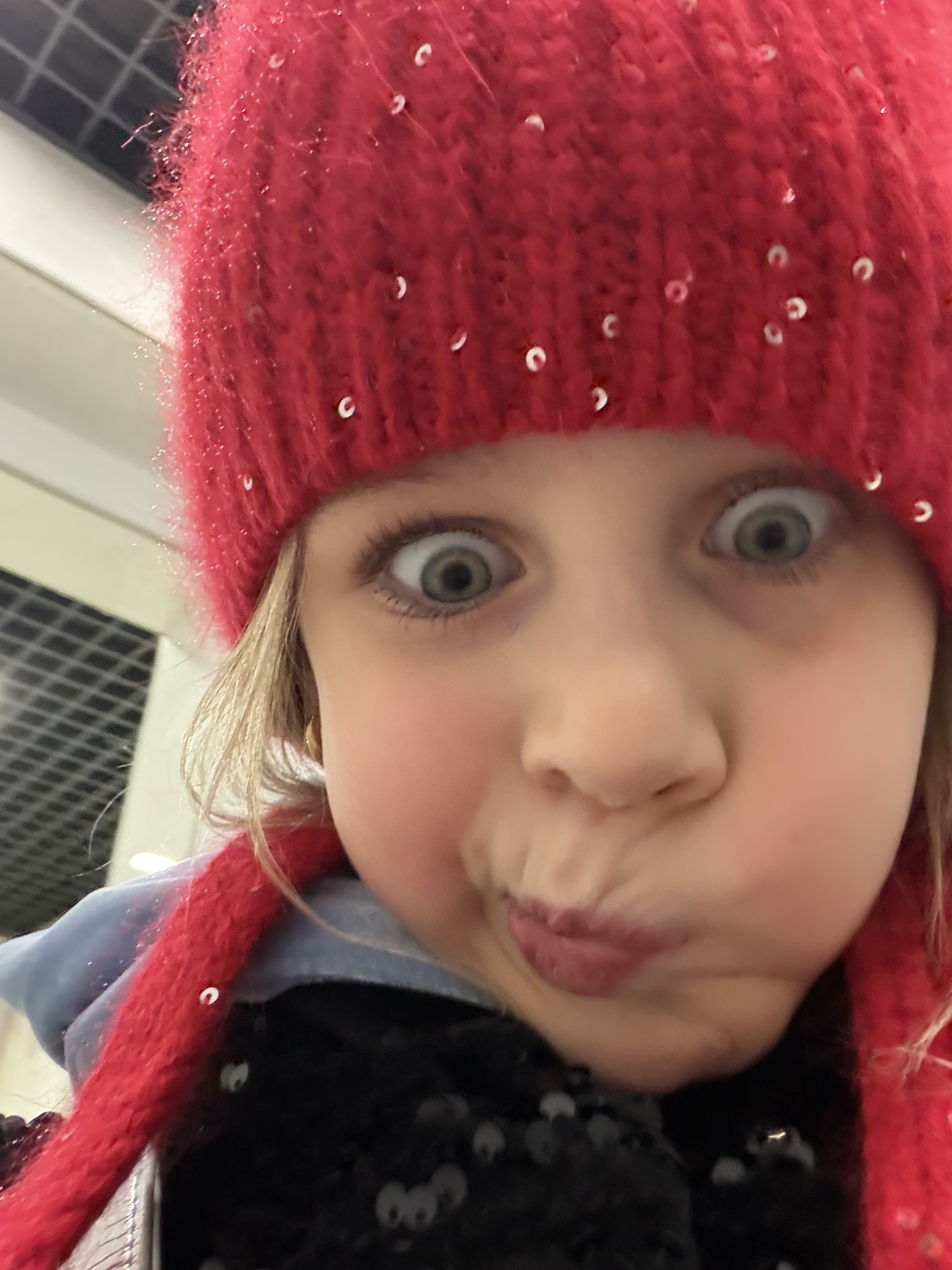 Милый портрет ребёнка в красной шапке с забавным выражением лица.