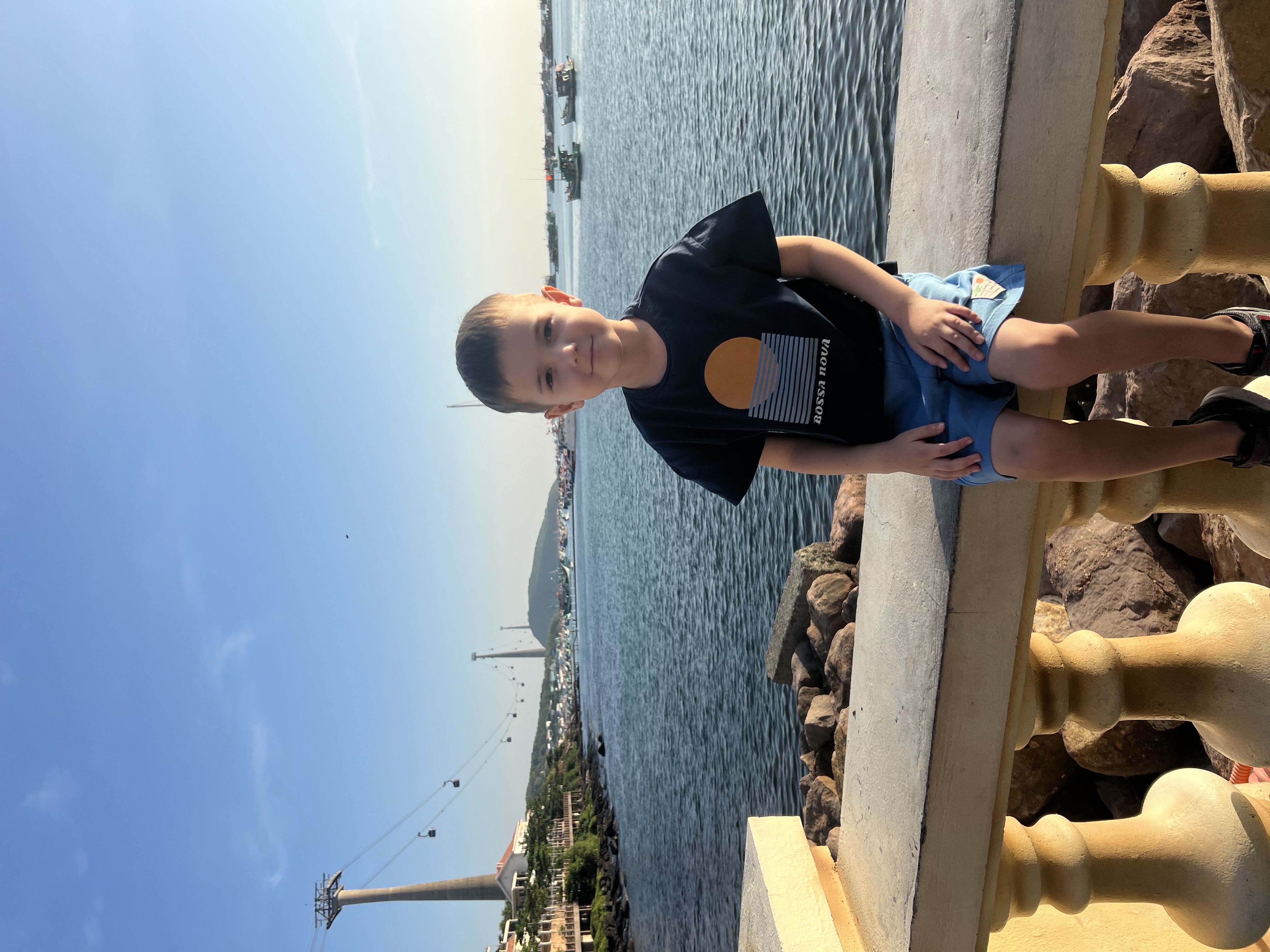 Мальчик сидит на балюстраде у воды на причале.