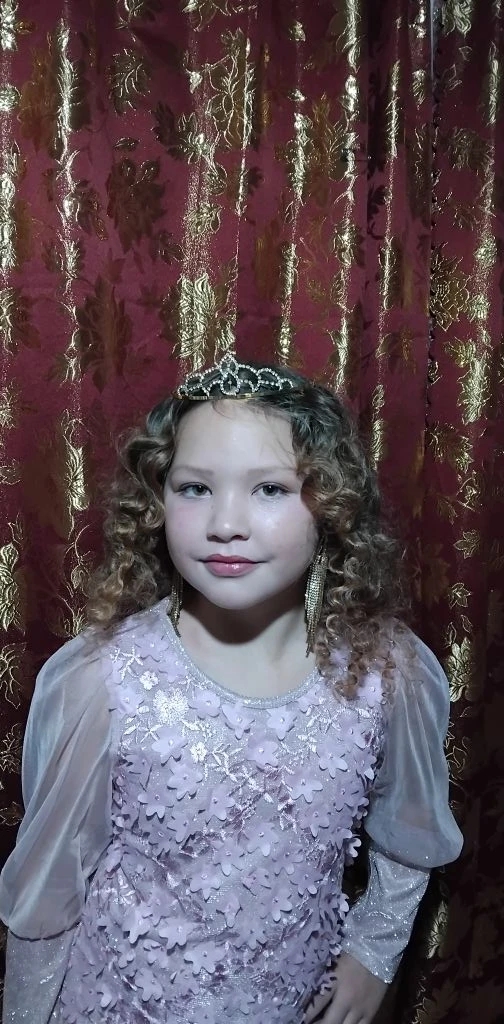 Маленькая девочка в розовом платье с диадемой на фоне бархатной ткани.