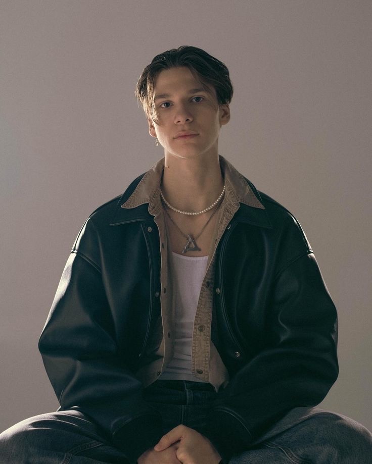 Молодой человек в кожаном пиджаке сидит на нейтральном фоне