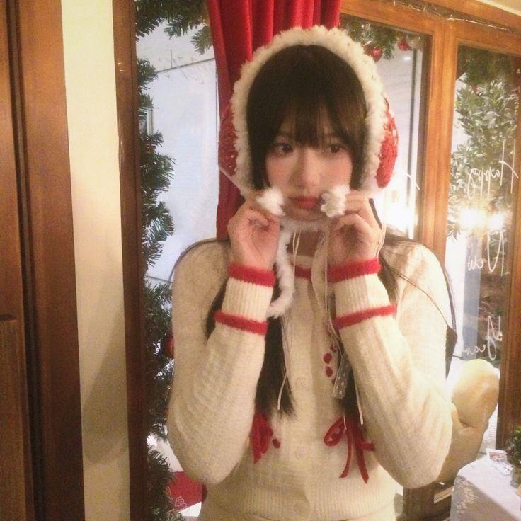 Молодая женщина в праздничной шапке и уютном свитере держит шарфик под подбородком, в атмосфере праздника.