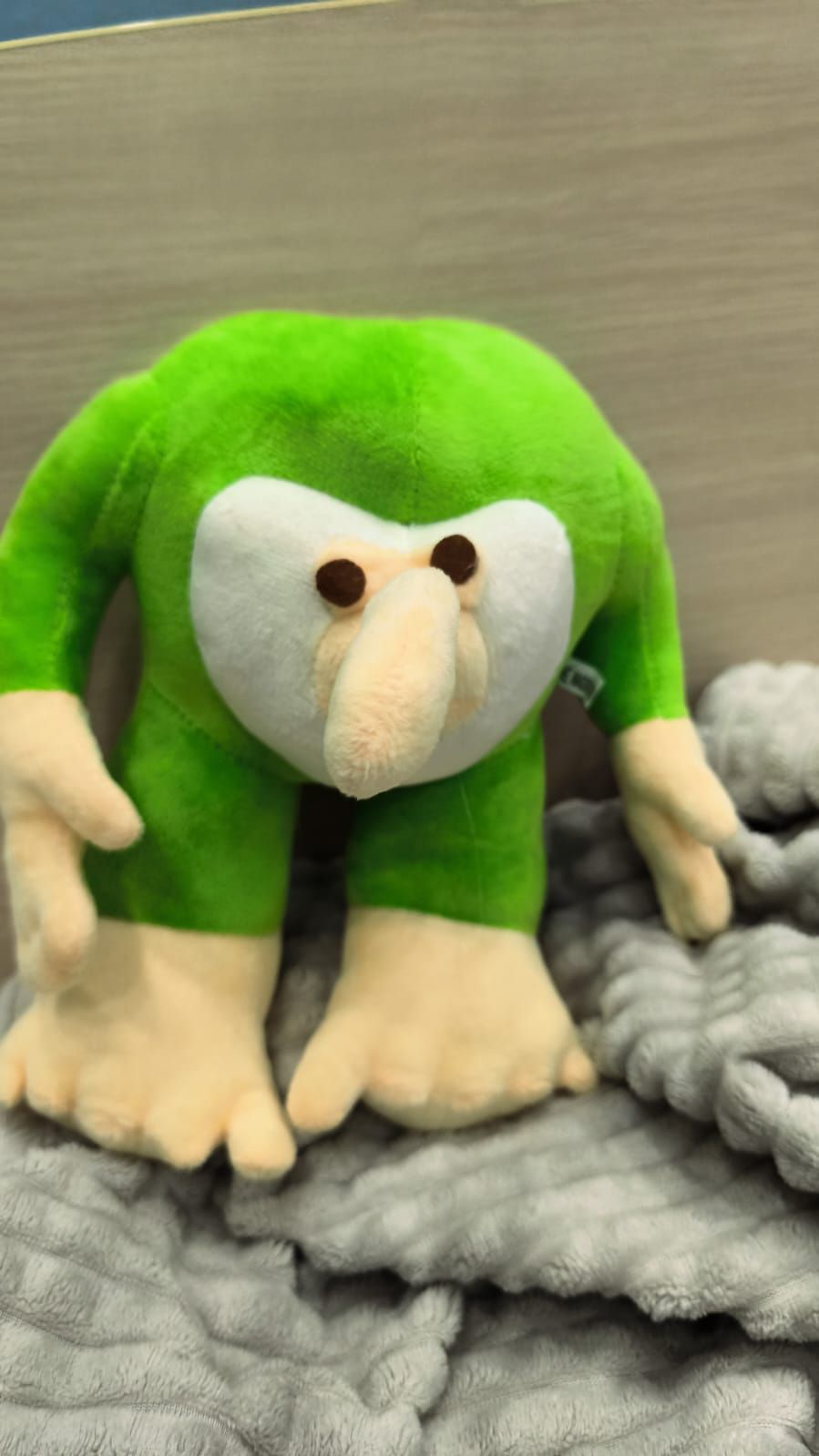 мягкая игрушка зелёного цвета с длинным носом на сером пледе