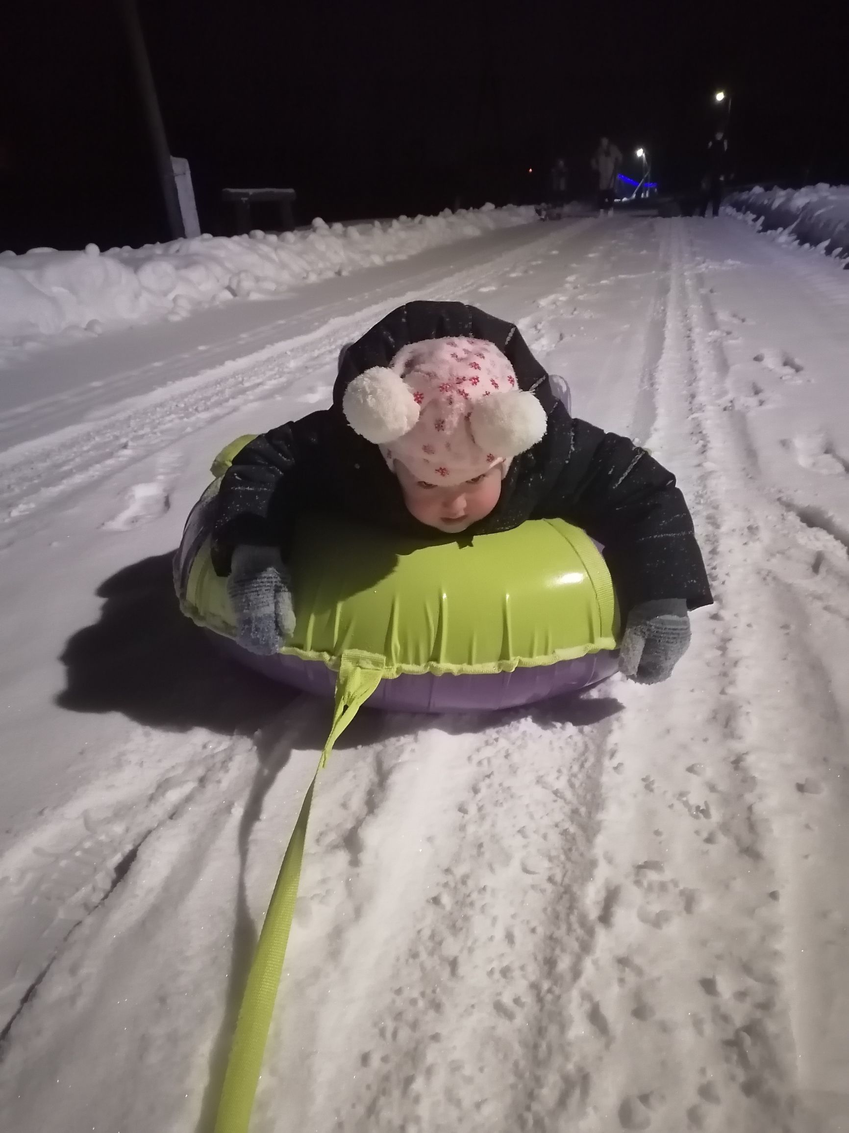 Ребёнок на надувной санке на заснеженной дороге ночью