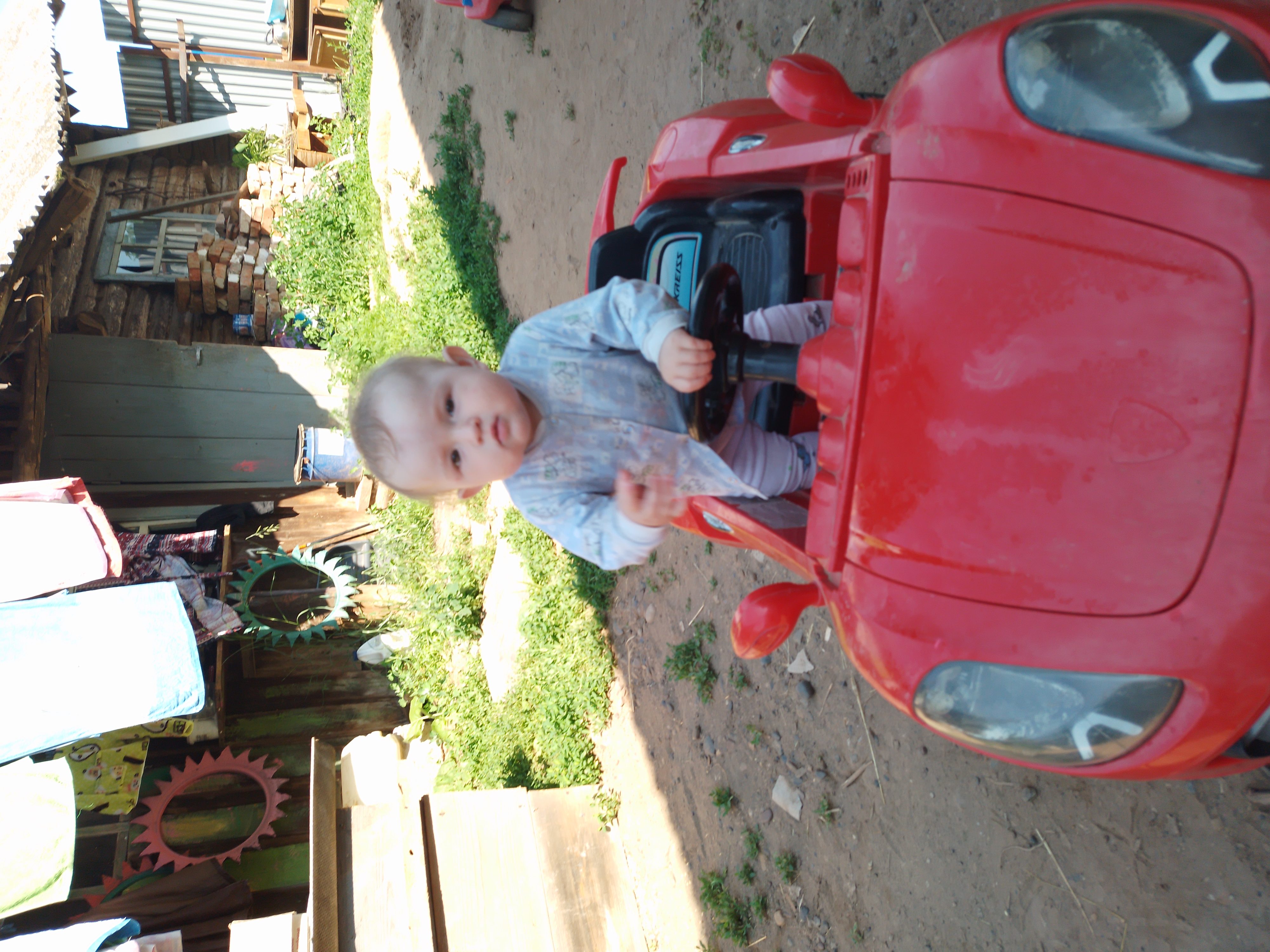 Малыш сидит в красной детской машинке на улице