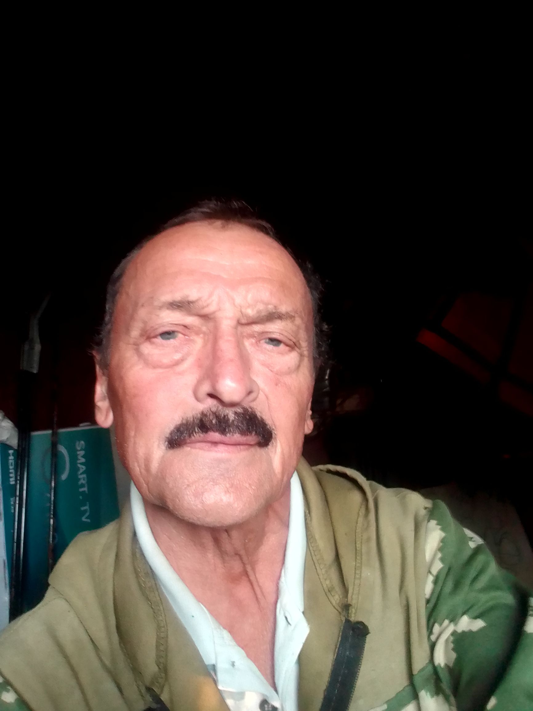 Фото пожилого мужчины в камуфляжной куртке на темном фоне