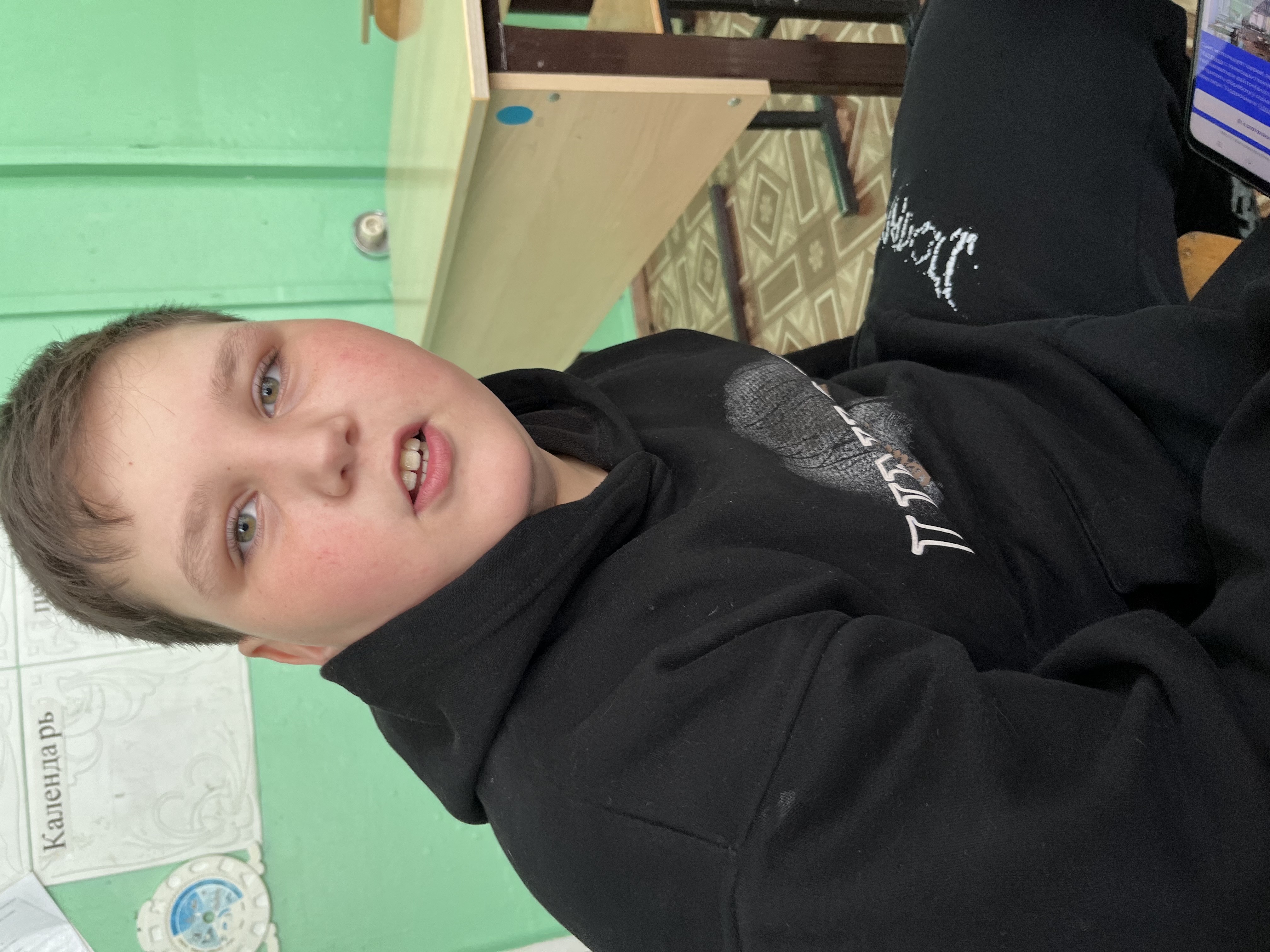 Подросток в черной толстовке сидит в помещении