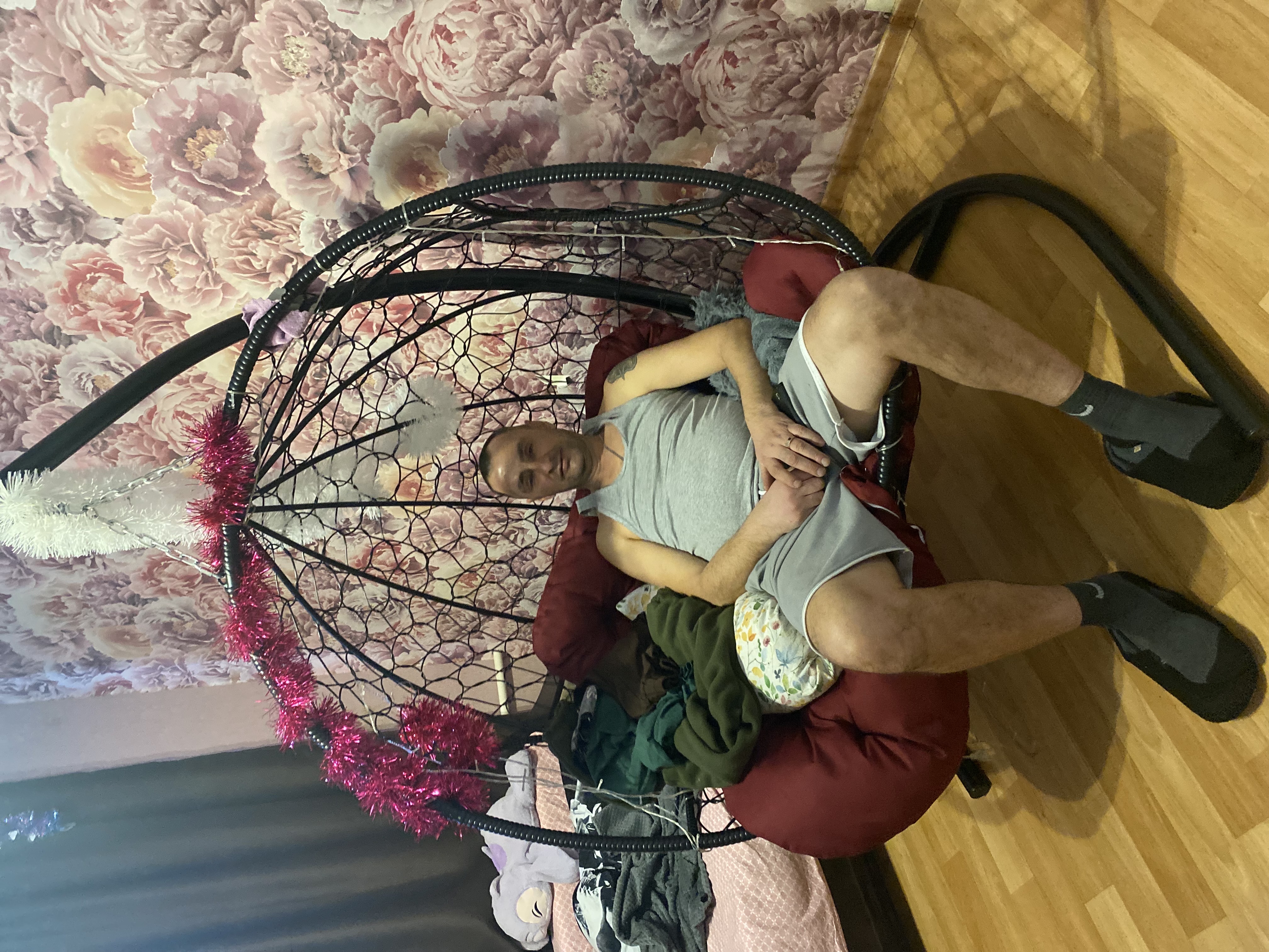 Мужчина в домашней обстановке сидит в подвесном кресле с ребенком на коленях.