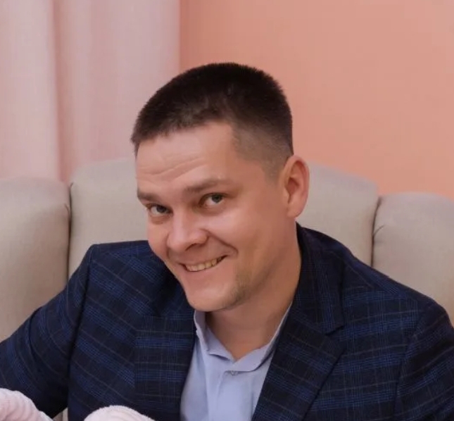 Мужчина в костюме улыбается на фоне розовой стенки