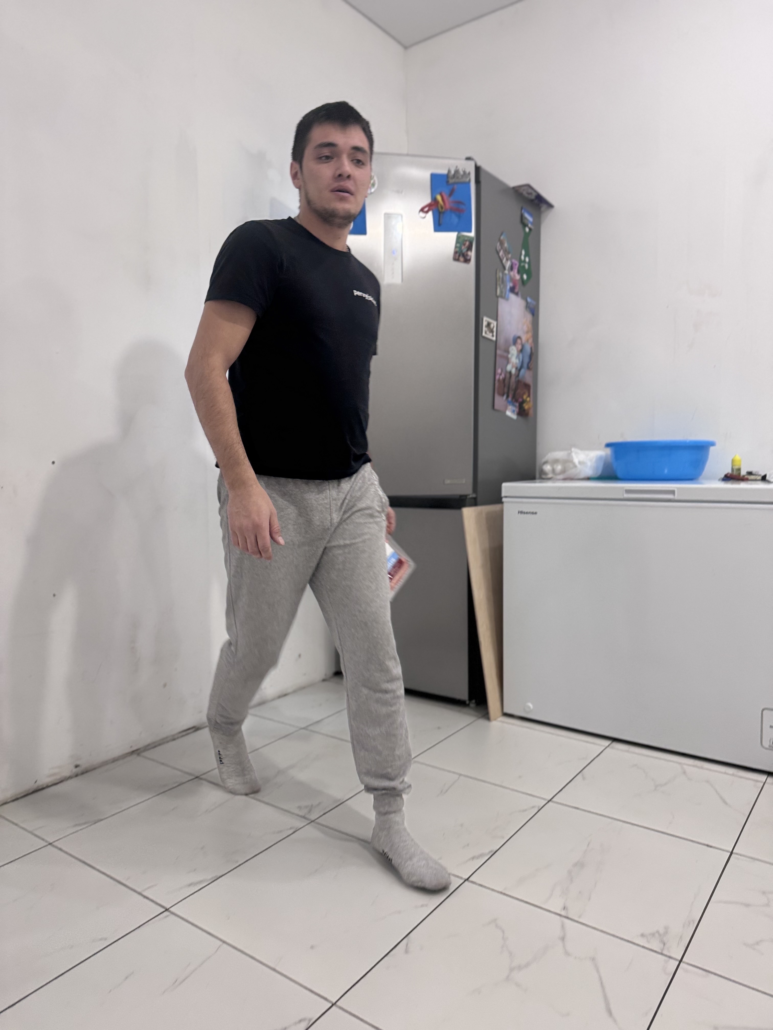 Мужчина в черной футболке стоит в белой кухне.